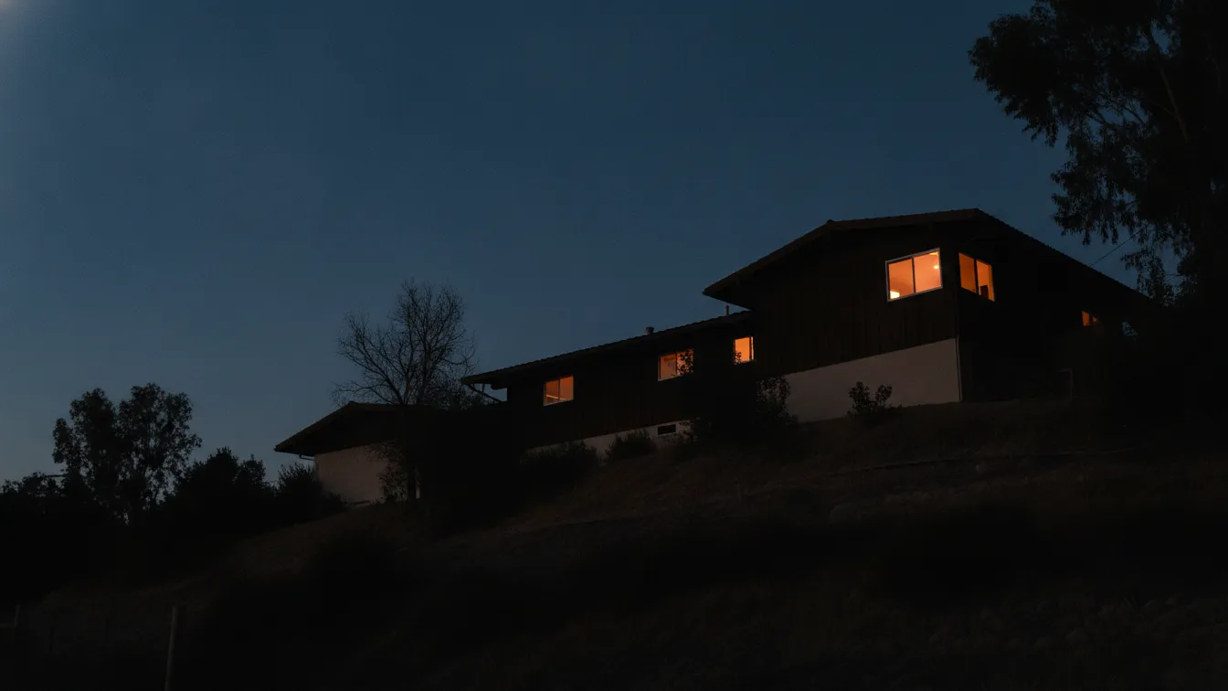 A Los Angeles house roofline at blue hour with one lit window